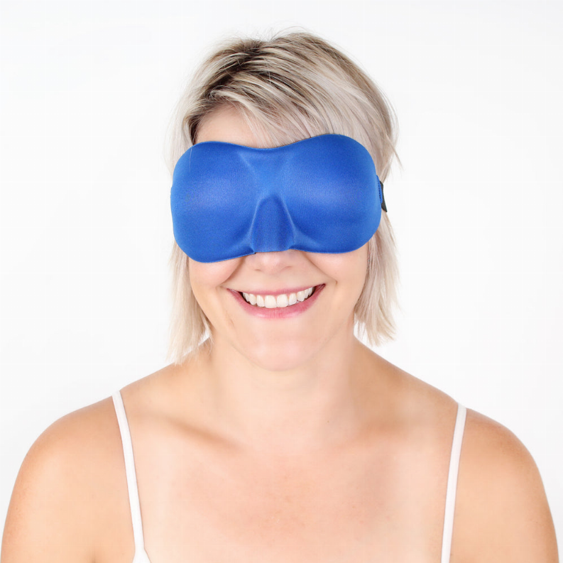 Blue soft sleep eye mask covering eyes, worn by a smiling person