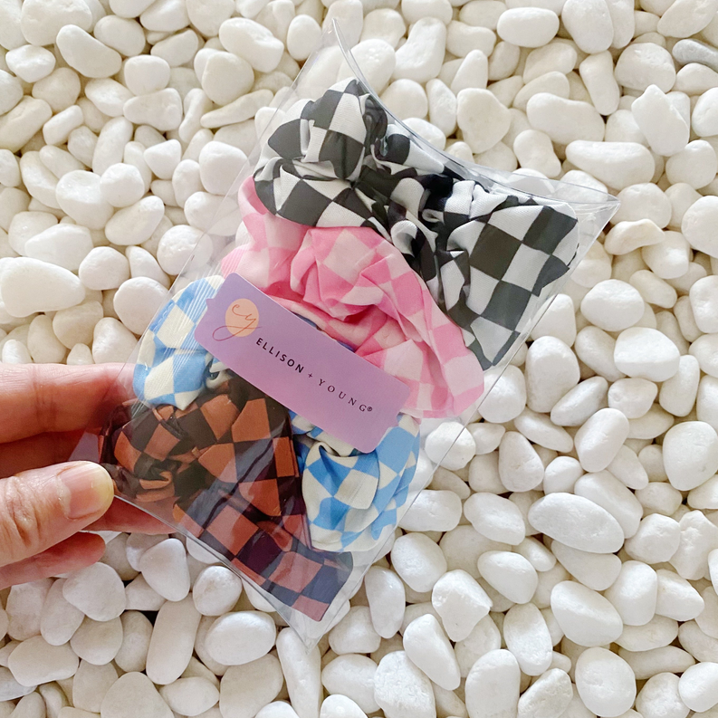 Clear bag with 4 checkerboard hair scrunchies; label shows black, blue, pink, brown.