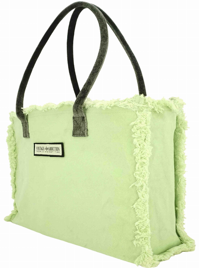Light green tote bag with black handles, fringe trim, and a small front label.