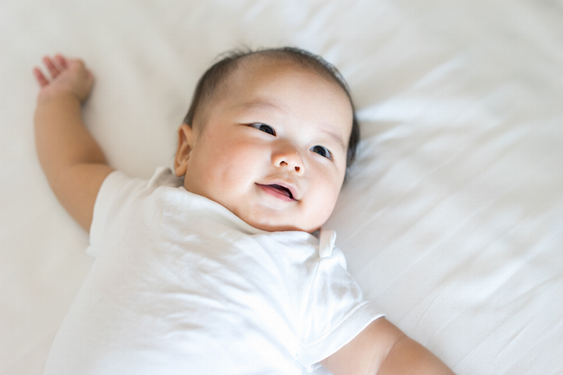 Baby in a white onesie with arms raised, smiling