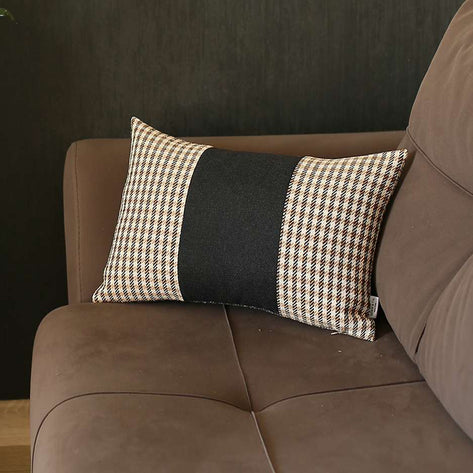 Rectangular throw pillow with black center panel and tan grid side panels beside sofa.