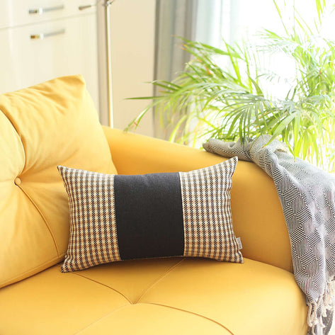 Rectangular throw pillow with black center panel and tan grid side panels on yellow couch.