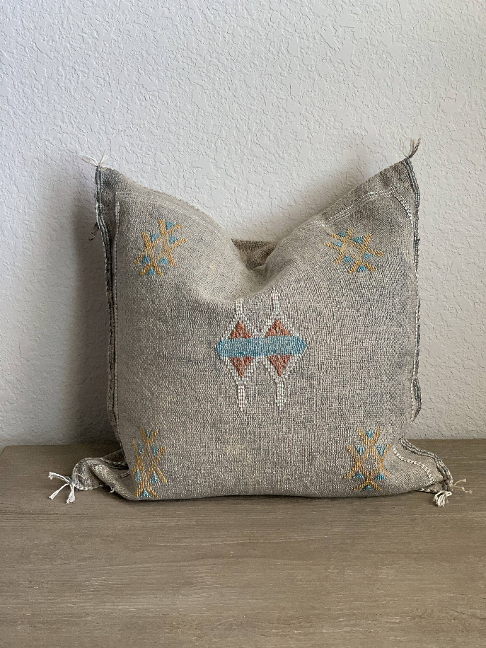 Gray handmade pillow cover with central hanging-figure motif, colorful embroidery, tassels