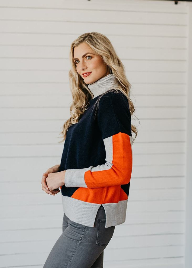 Color-block turtleneck sweater side view, dark navy with orange sleeve and light gray ribbing