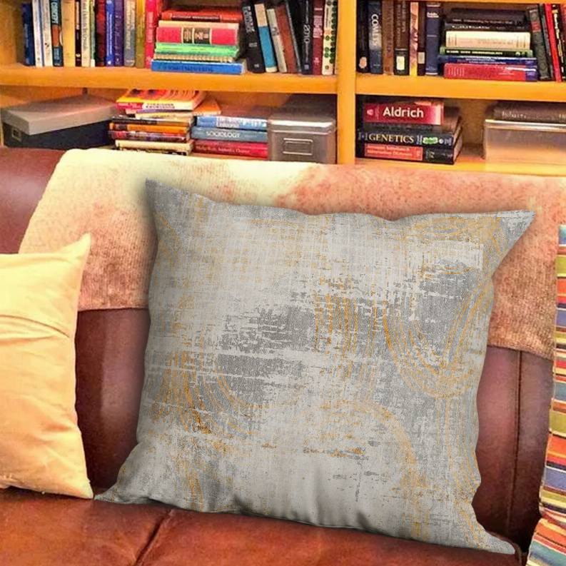 Square decorative throw pillow in light gray with gold abstract lines, textured weave