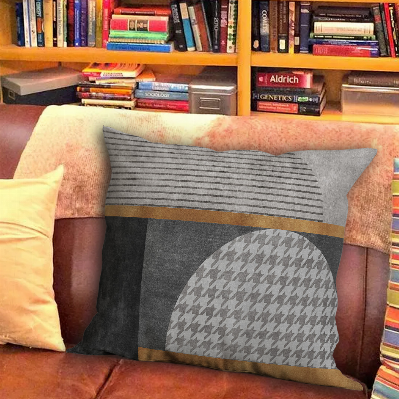 Square decorative pillow with dark gray striped top, houndstooth lower circle, gold stripe