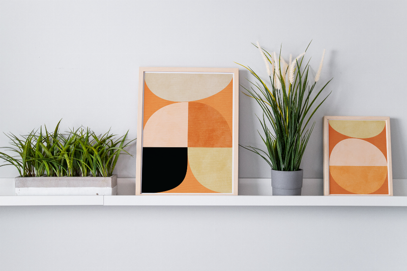 Two framed abstract wall art prints with terracotta, beige, and black shapes on shelf