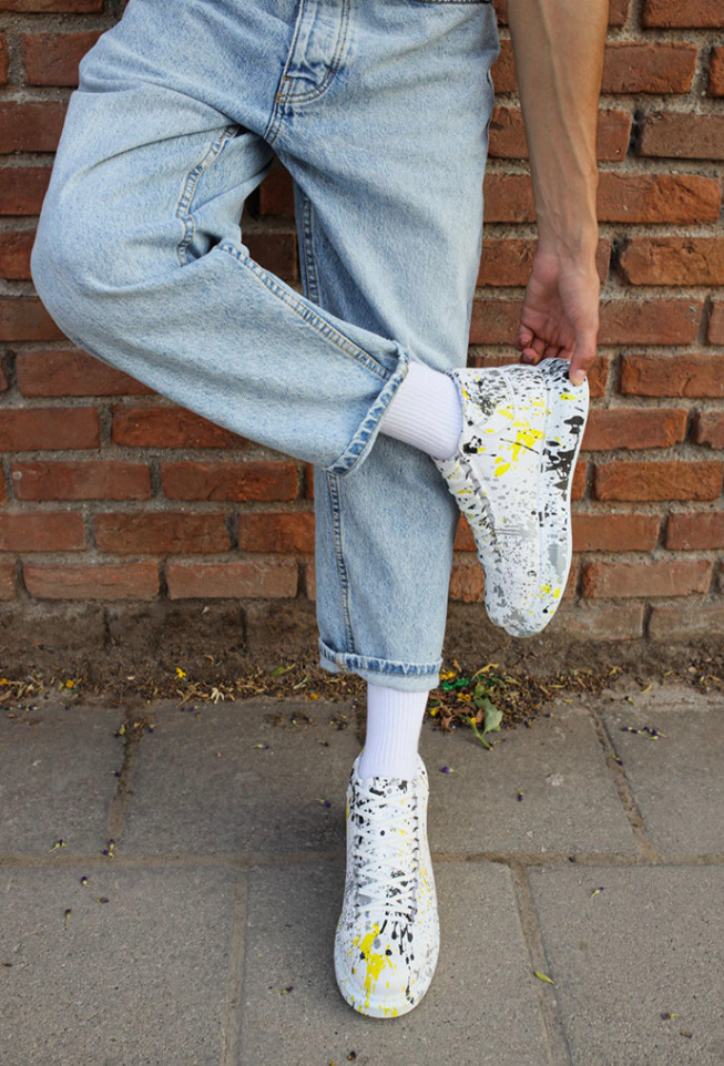 White high-top sneakers with yellow and black splatter, ankle socks visible