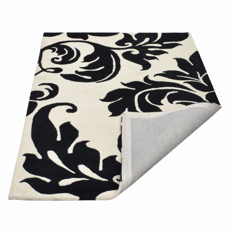 Black and ivory floral area rug with ornate swirls, corner with gray backing
