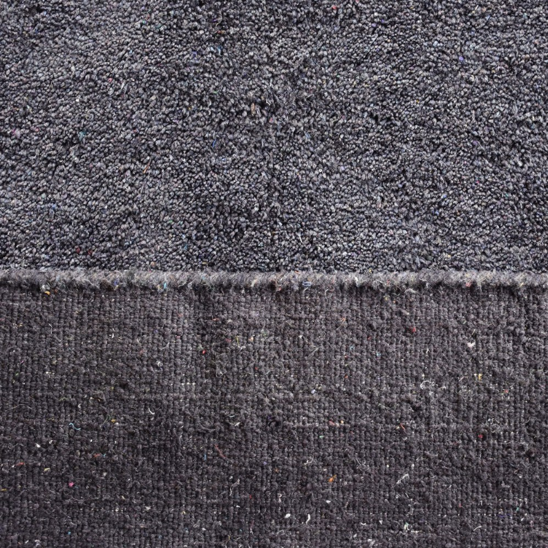Dark gray area rug surface close-up with fringe edge and speckled high-pile texture