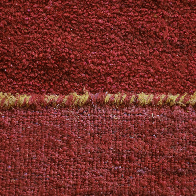Rug pile close-up in deep red with a narrow gold border stripe along the edge.