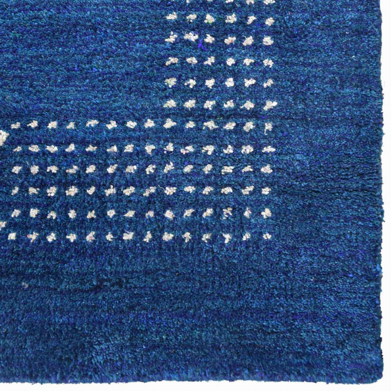 Blue area rug detail with cream dot-squares forming curved horizontal bands.