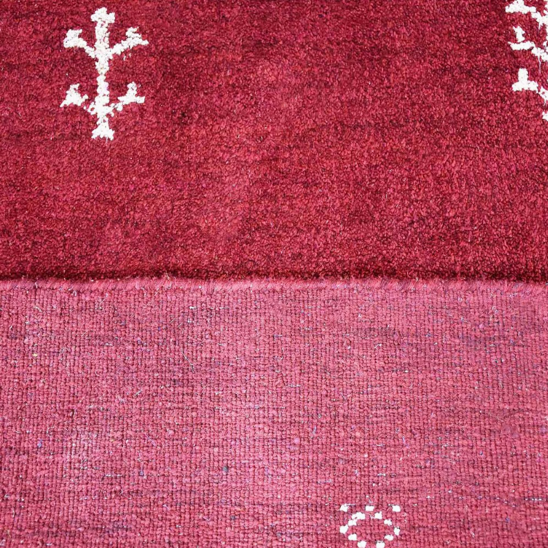 Red area rug close-up showing edge seam and light backing beneath white motifs