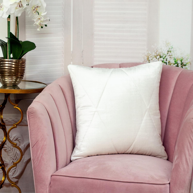 White quilted throw pillow with stitched channels on a pink velvet armchair