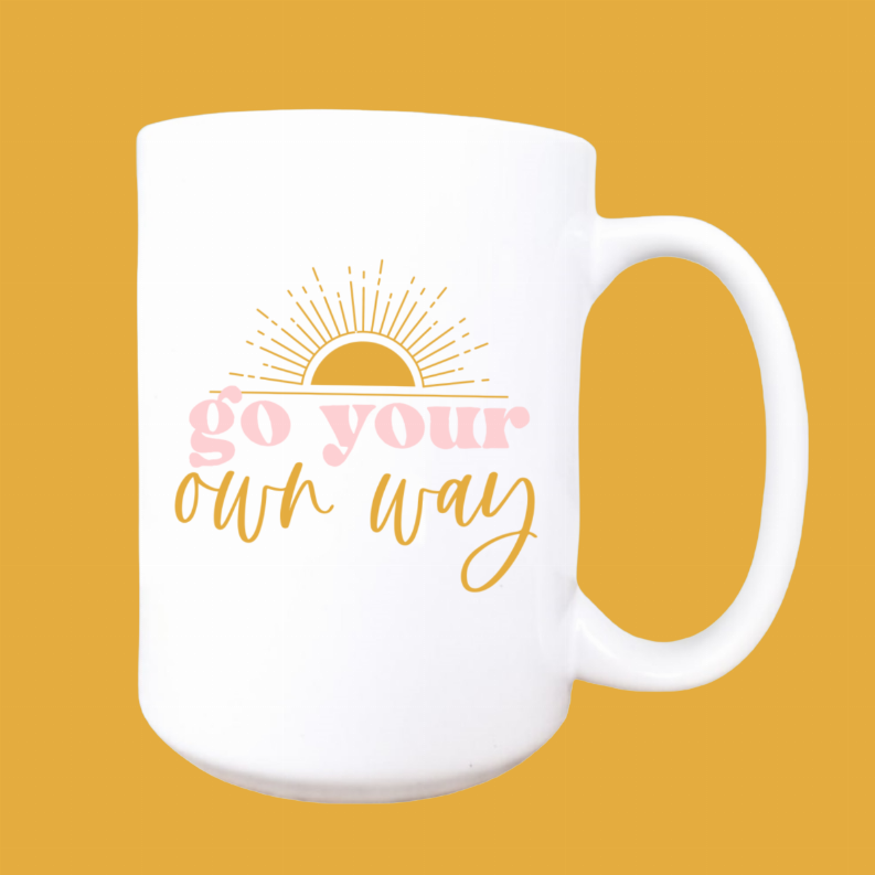 White ceramic coffee mug with pastel 'Go your own way' lettering and sun rays