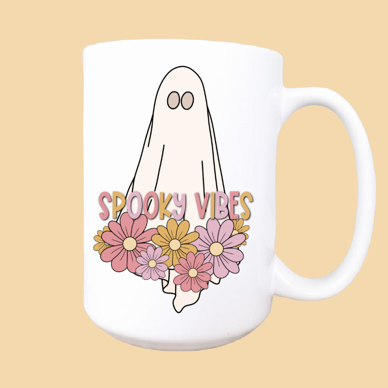 White mug front with handle, ghost face above floral art and 'Spooky vibes' lettering