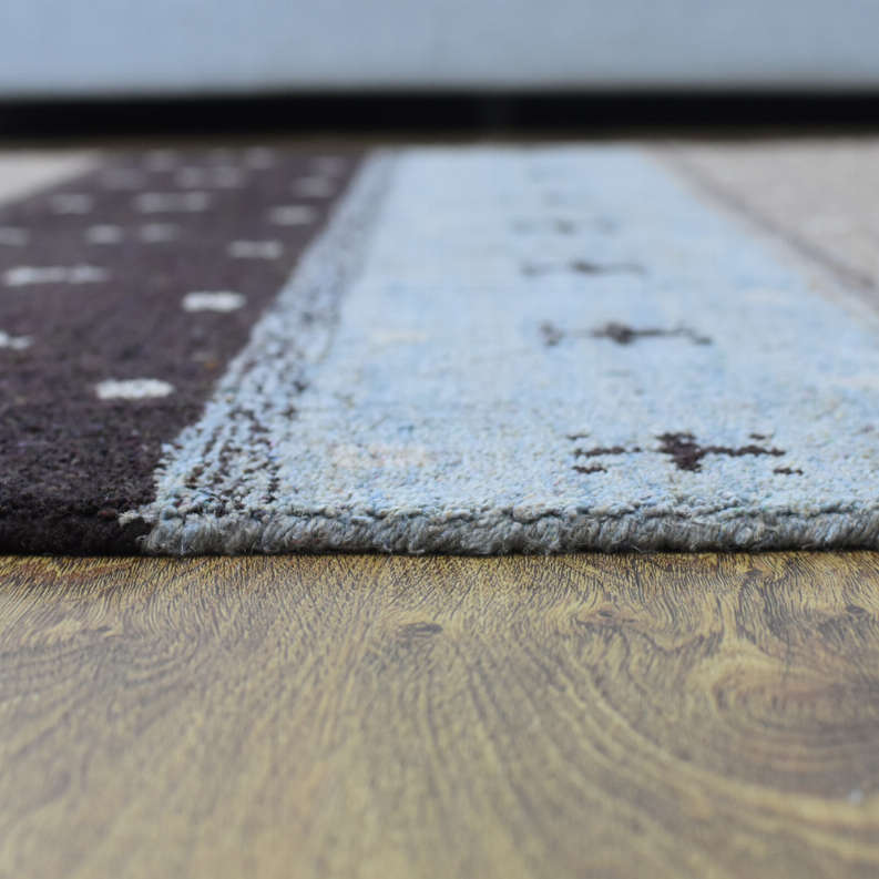 Area rug edge with short textured pile and cream pattern blocks near the border.