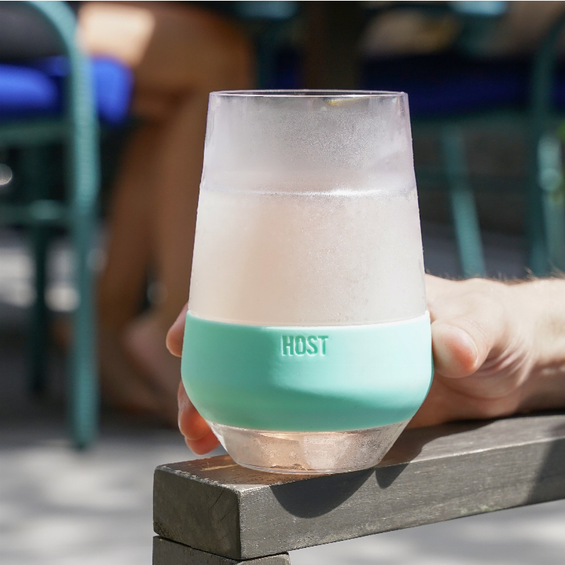 Wine cooling cup on wood block, held hand, clear body with mint band, frosty surface.