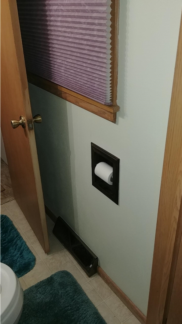 Recessed toilet paper holder in wood trim with toilet paper roll behind wall