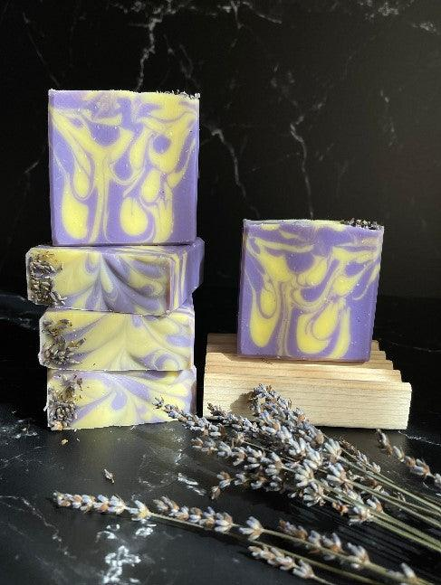 Purple and yellow swirled lavender lemon soap bars on light wood with dried lavender