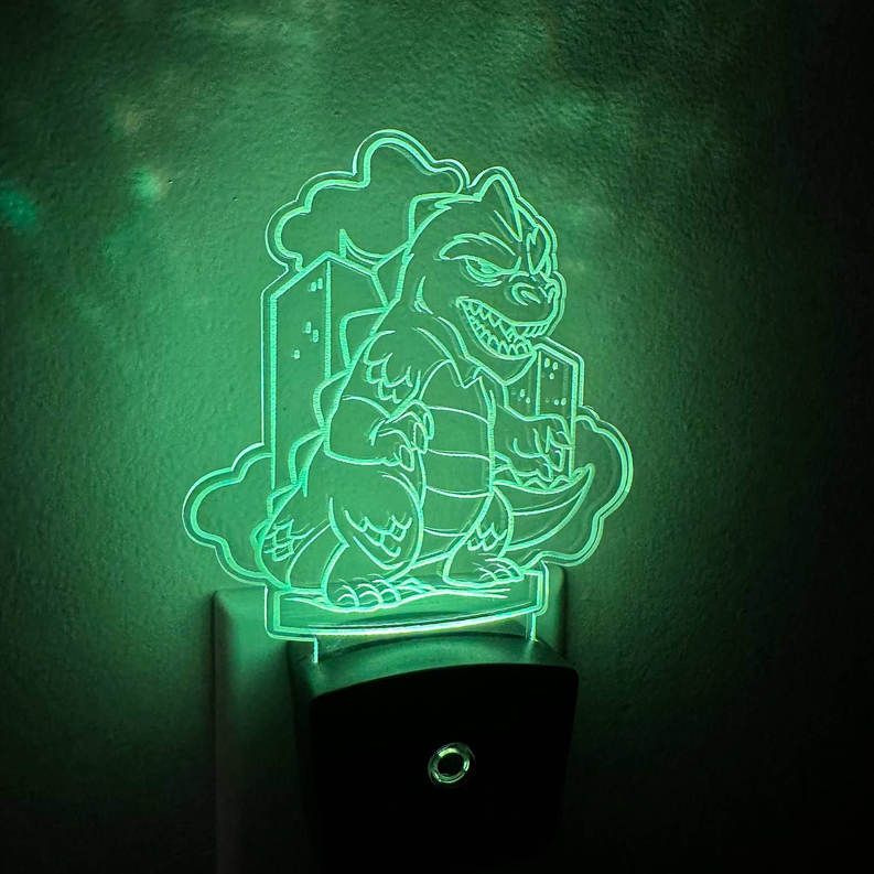 Plug-in LED night light with glowing green kaiju outline on black base