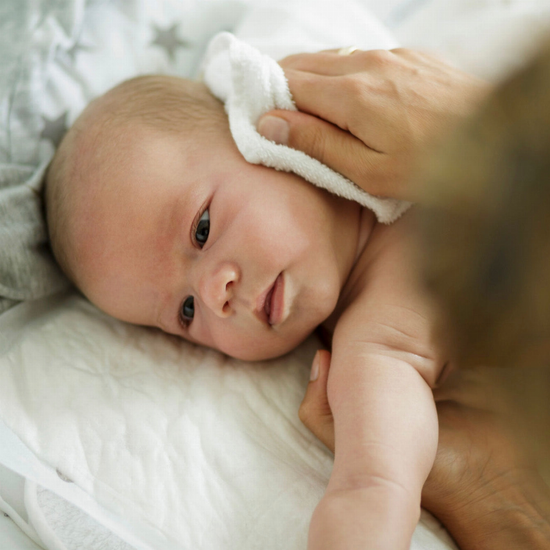 Baby being gently dried with a soft white towel on a cozy gray bedspread, showcasing a serene moment.