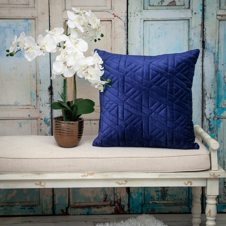 Blue geometric quilted throw pillow on a sofa with floral decor nearby