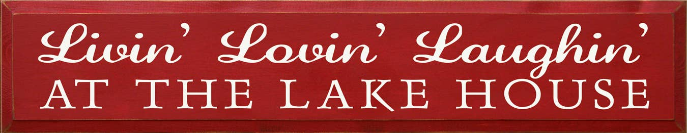 Red wood sign with white cursive 'Livin' Lovin' Laughin' and 'AT THE LAKE HOUSE'