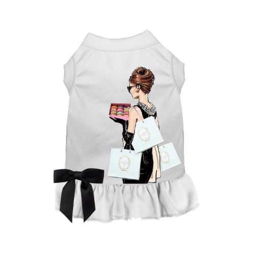 White dog dress with sleeveless cut, ruffled hem, black bow, and illustrated lady holding macarons