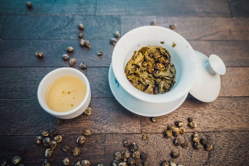 White bowl of jasmine tea pearls with small cup on wooden surface