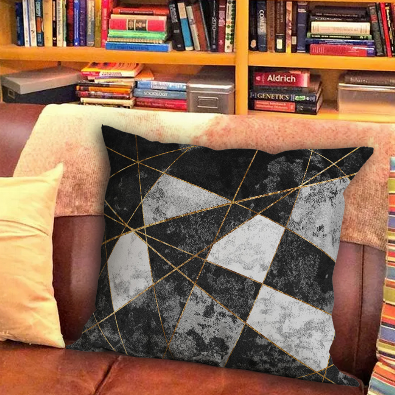 Geometric decorative pillow in black, gray, and gold on a brown couch