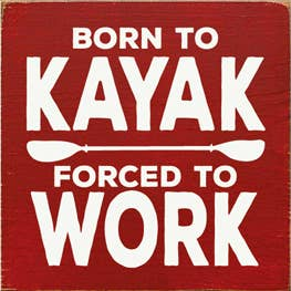 Red wooden sign with bold white text: 'BORN TO KAYAK' and 'FORCED TO WORK'.