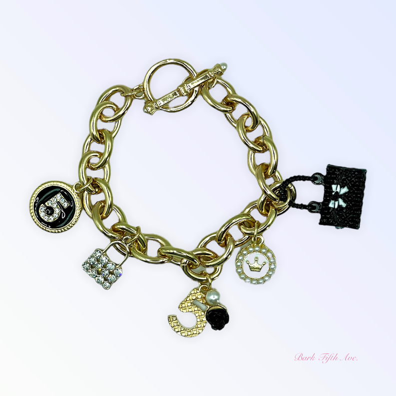 Gold-tone charm bracelet with black square charm, round medallion, heart, and crystal charms