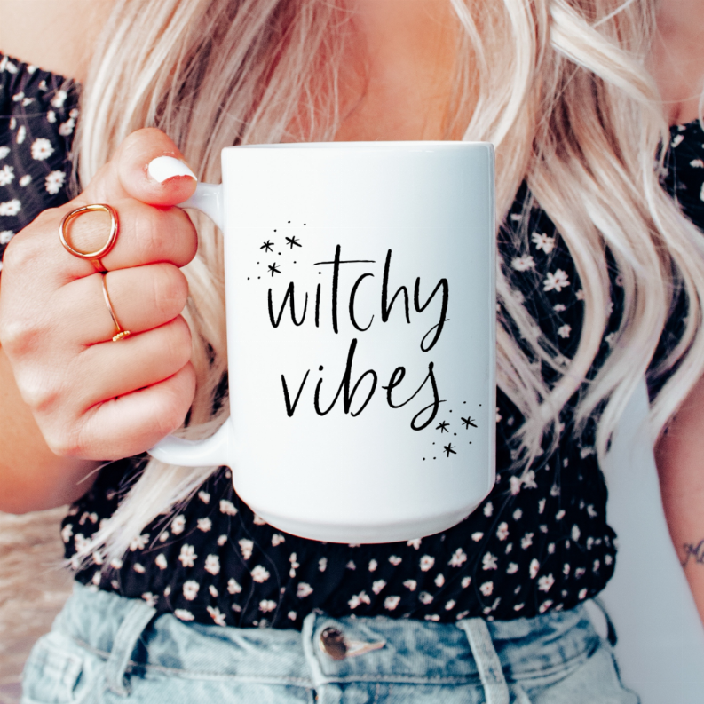 White ceramic coffee mug with black "Witchy Vibes" lettering and star sparkles