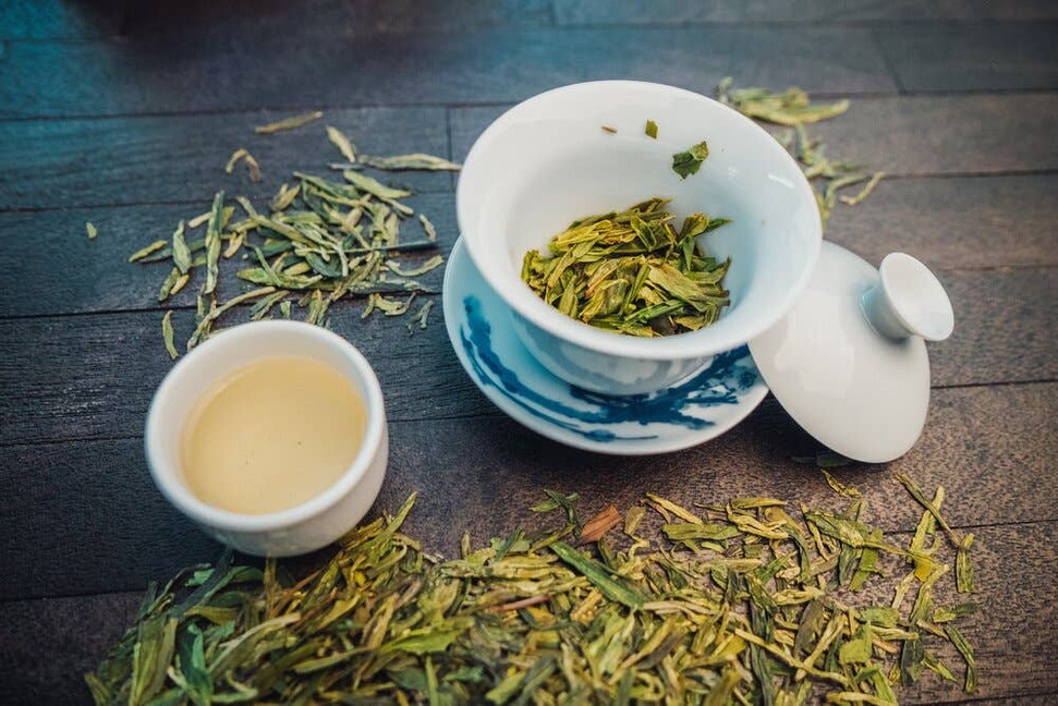 Organic Dragonwell tea in white cups with loose green leaves and a small filled cup