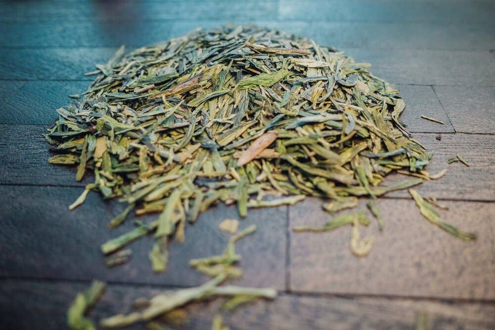 Organic green tea leaves in a close-up pile on dark wood