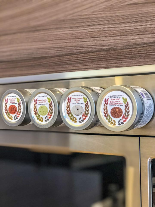 Four seasoning jars with metallic lids lined up on a kitchen shelf