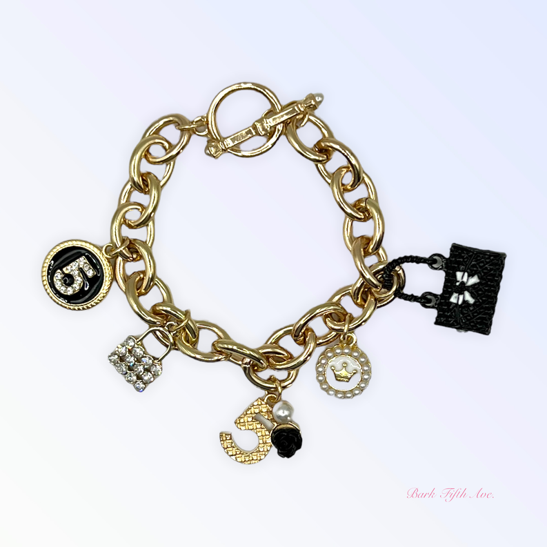 Gold-tone charm necklace with lobster clasp, circular pendant, rhinestone heart, and black bow