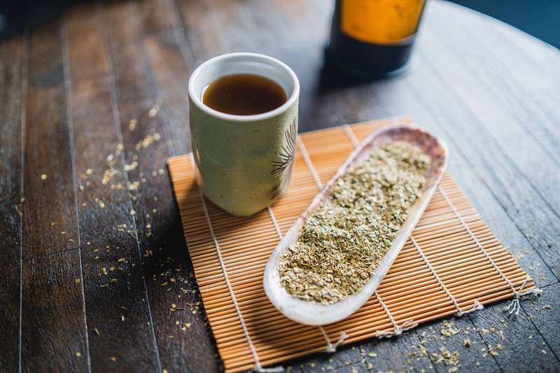 Green mate cups and white spoon filled with green yerba mate leaves on mat