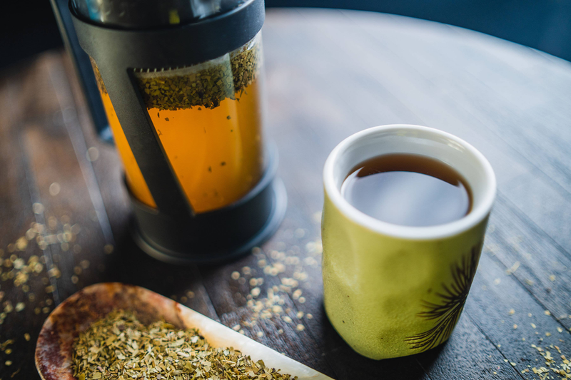 Metal mate container and green cups with scattered yerba mate leaves on tabletop