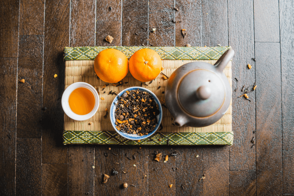 Organic royal orange spice blend in bowl with oranges, tea cup, and teapot