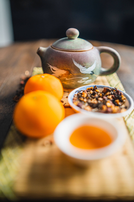 Orange spice blend in ceramic bowl, with teapot and oranges nearby