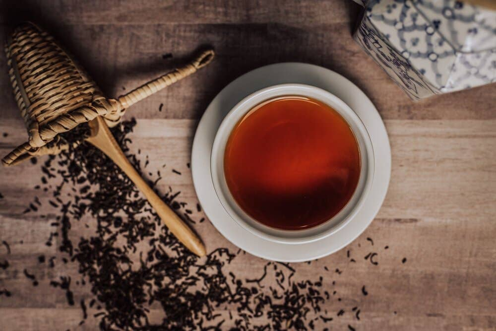 Cup of dark elderberry tea with scattered dried herb on a wooden surface