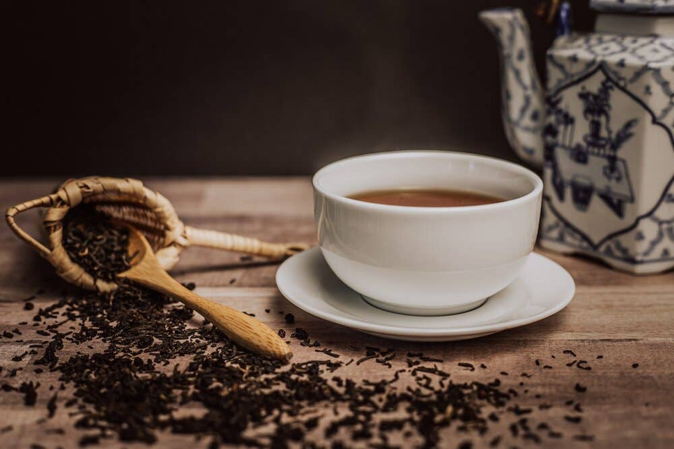 White cup and saucer filled with dark elderberry tea, with dried herbs nearby