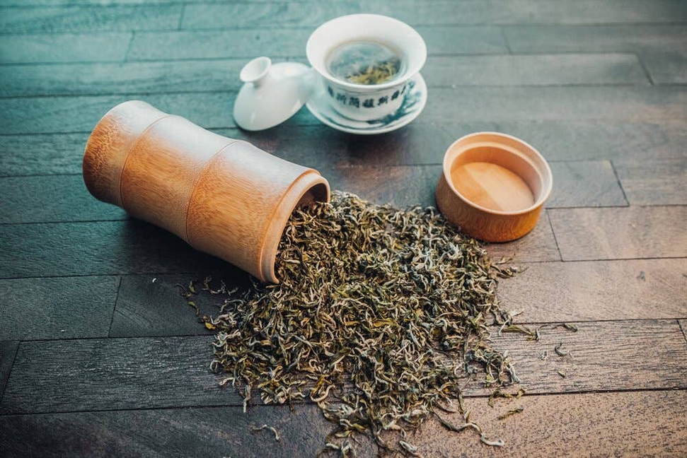 Loose dark green tea leaves with wooden scoop and small teacup