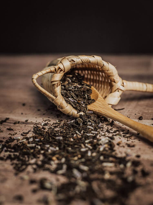 Woven basket with organic lavender tea leaves and a wooden scoop on a surface