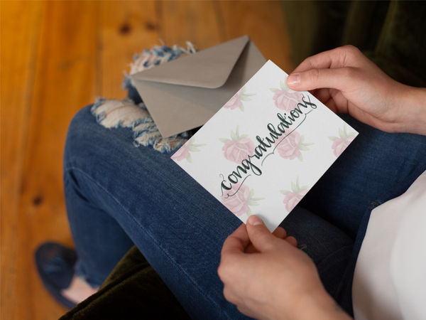 Floral congratulations greeting card in white with pink roses, held with envelope