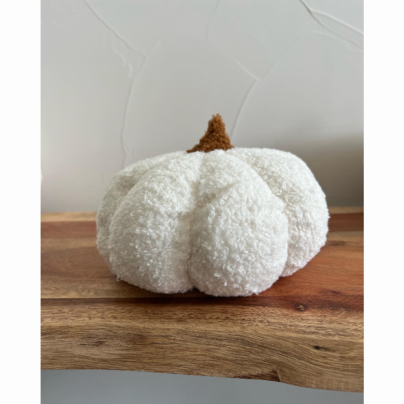 Boucle pumpkin throw pillow, white plush with brown stem, on a wooden surface