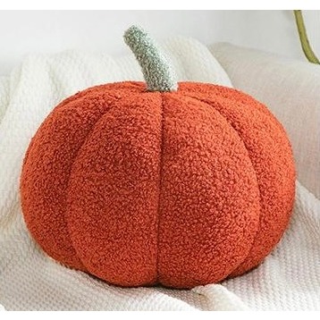 Orange plush pumpkin pillow with green stem on white quilted fabric