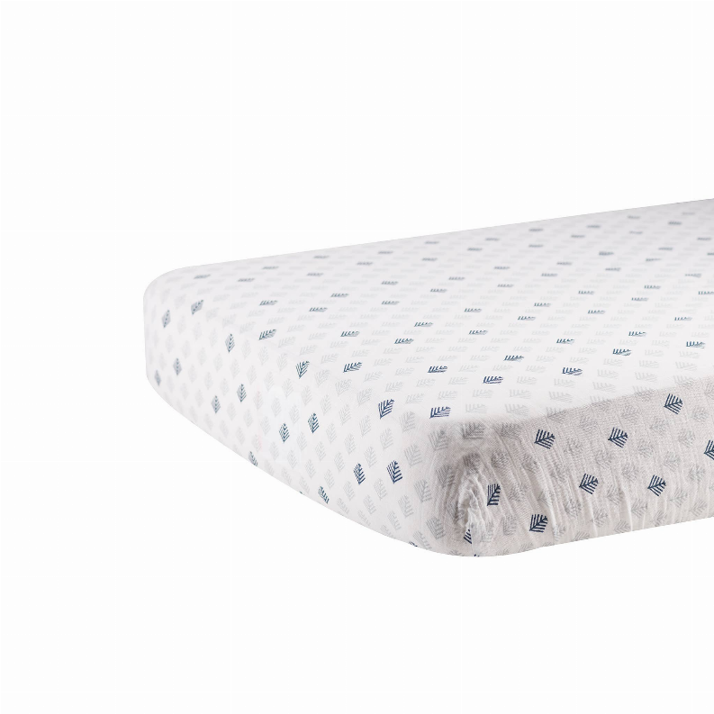 White crib sheet with scattered blue leaf prints, fitted corner seam visible